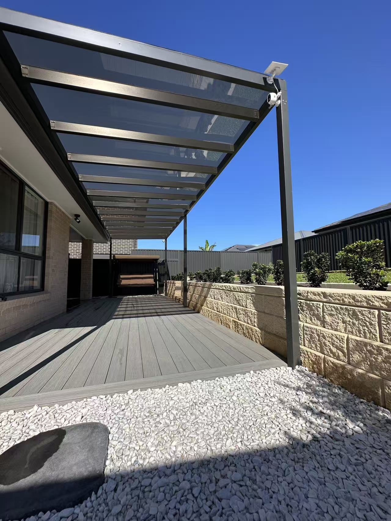 Outdoor patio area with a pergola and gravel pathway under a clear blue sky.