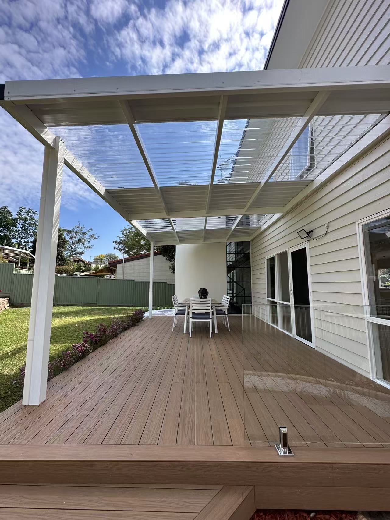 Wooden deck with glass patio cover and outdoor furniture under a clear blue sky.